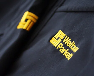Dunkelblaue Softshelljacke mit gelb gesticktem Logo von Weitzer Parkett