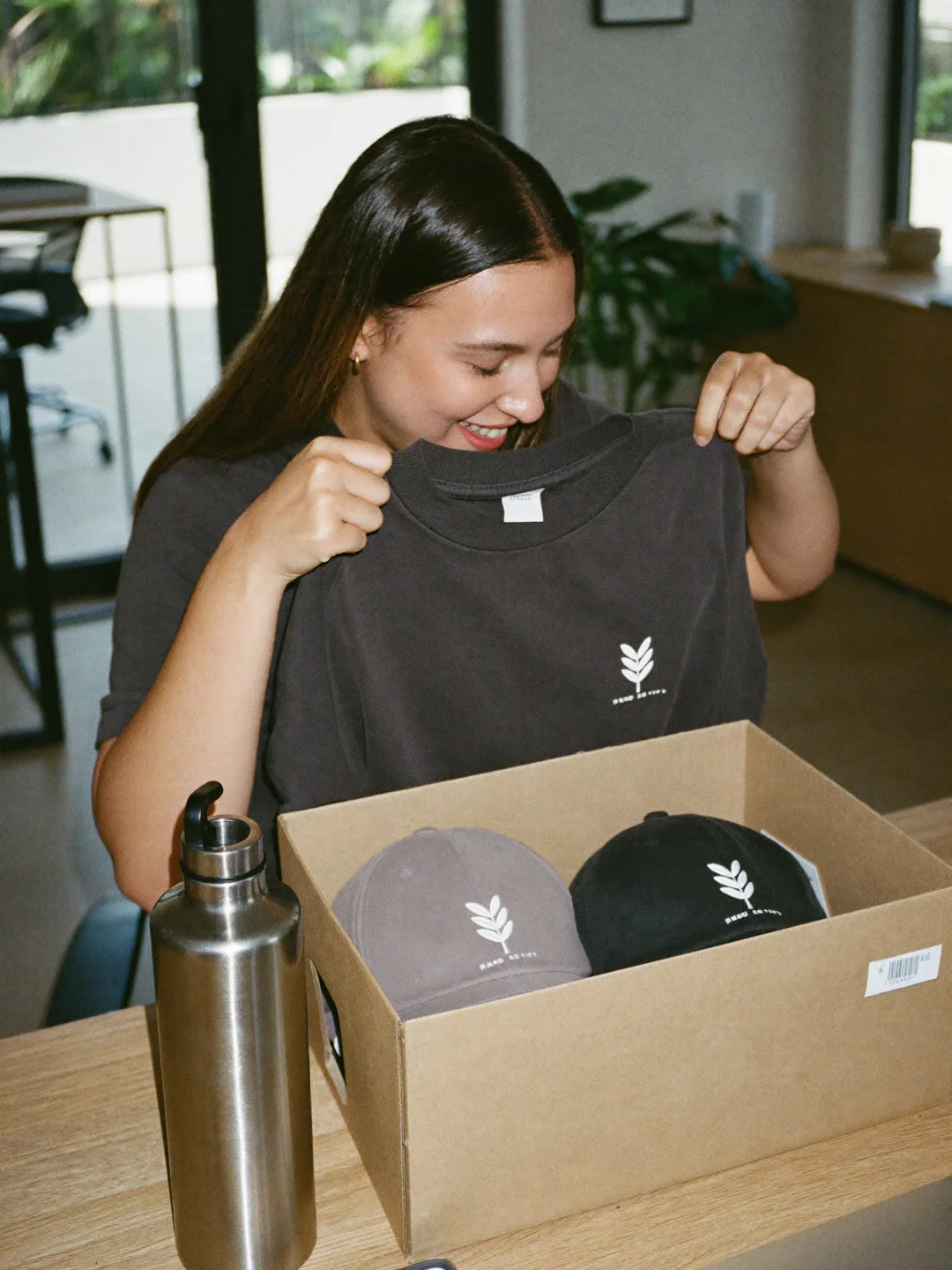 Neue Mitarbeiterin packt ihre Welcome Box mit Shirt und Kappen aus