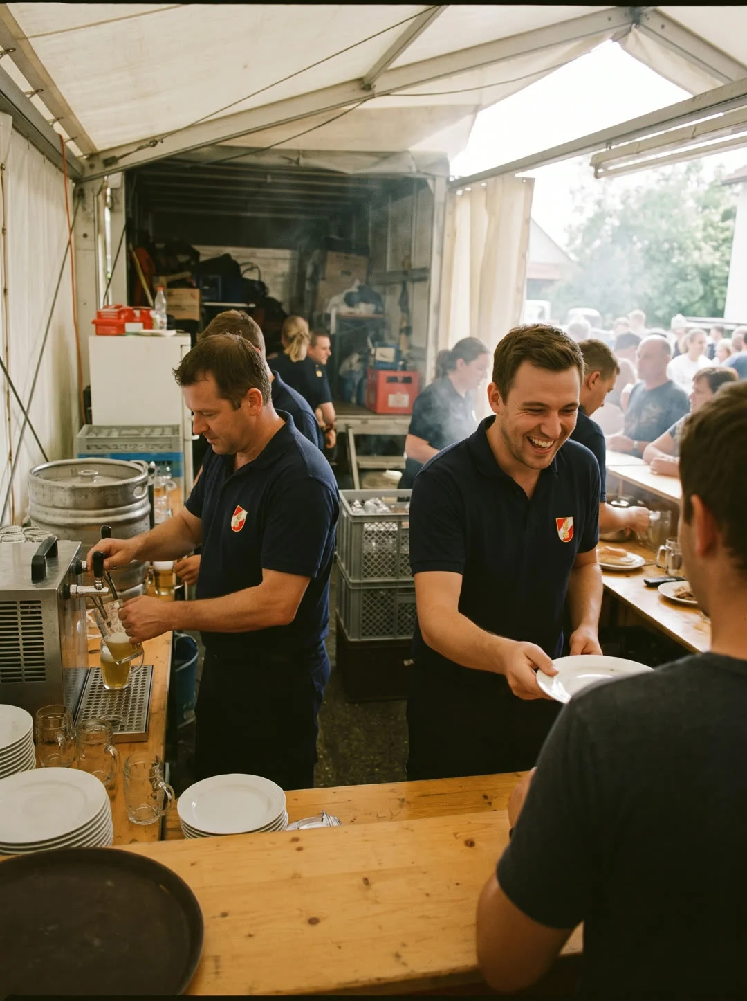 Feuerwehrmitglieder in Polos mit gesticktem Wappen schenken beim Sommerfest im Zelt Bier aus