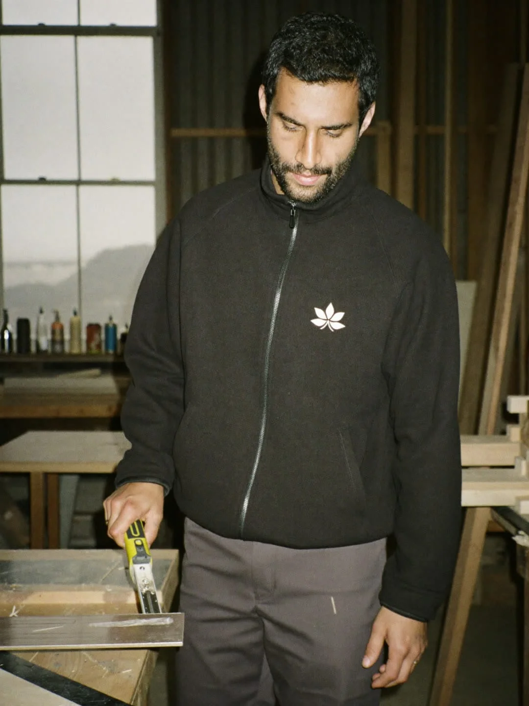 Tischler in schwarzer Arbeitsjacke mit gesticktem Emblem in der Werkstatt